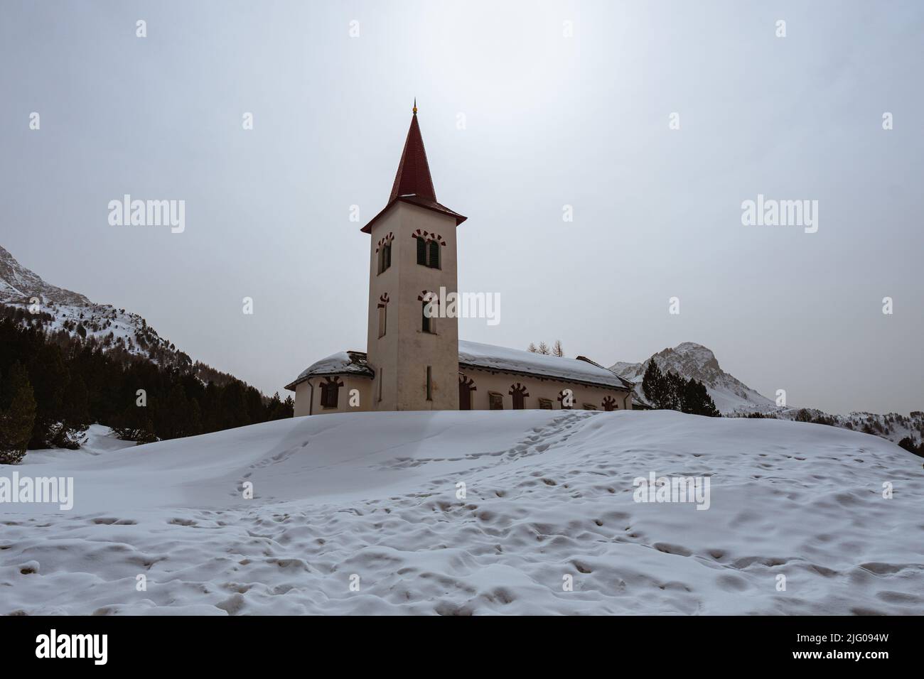 The white church, in the village of maloja, covered by snow during a late winter day, Switzerland - March 2022. Stock Photo