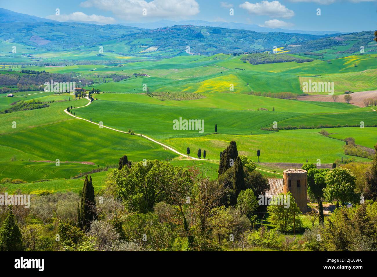 Tuscany, Italy. Val d'Orcia scenic rolling hills landscape panorama with blossoming rapeseed flowers and antique stone farmhouse with tower Stock Photo