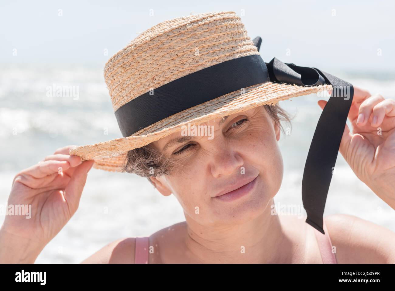 Portrait of gray-haired woman in a boater with a black ribbon philosophically thoughtfully watching something with little smile.Concept of femininity. Stock Photo