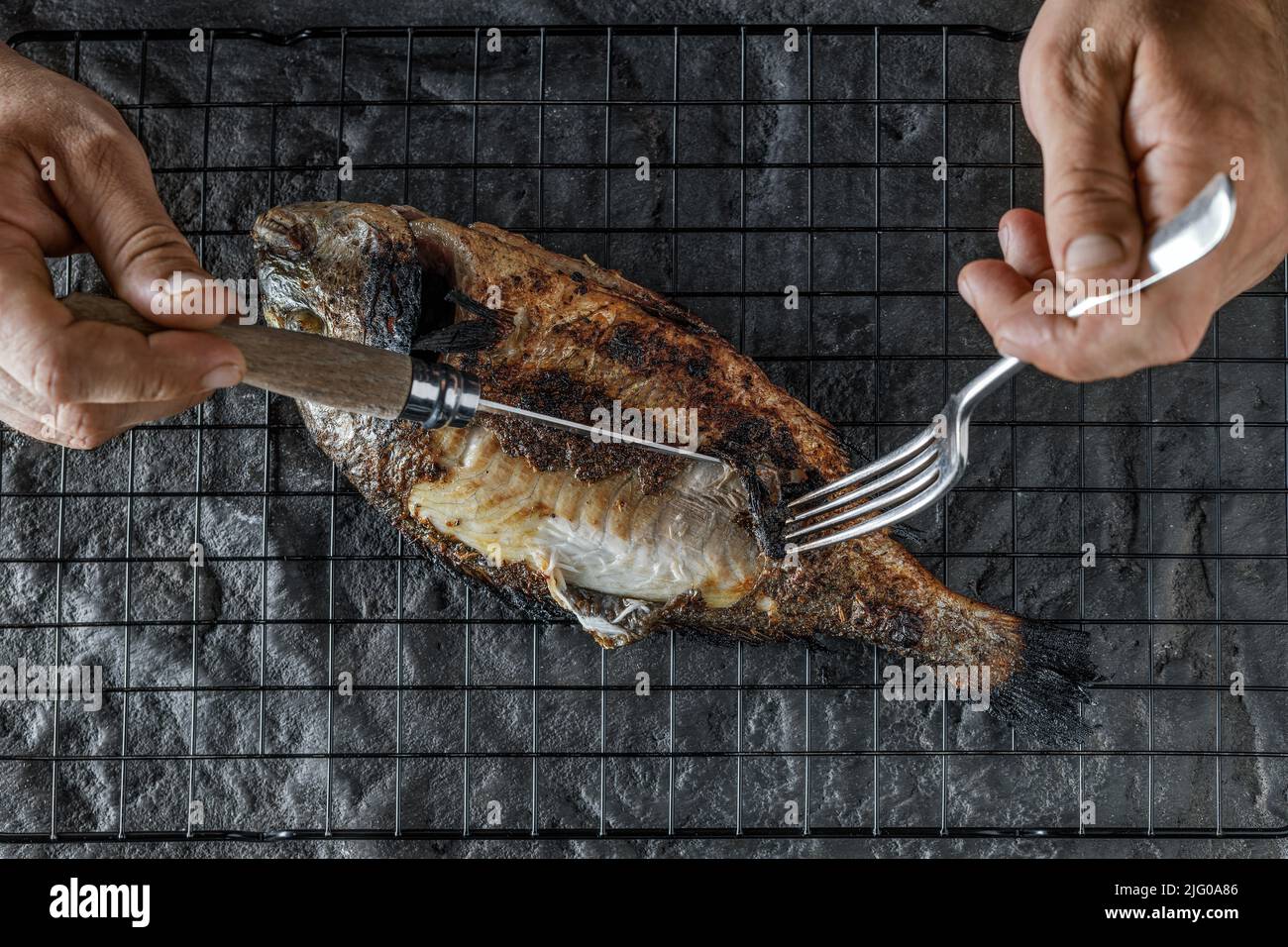 Eating whole grilled Dorado or Sea Bream on dark textured