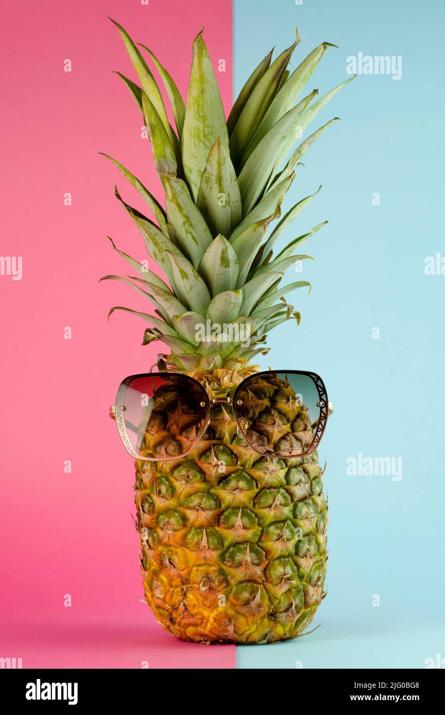 Pineapple with sunglasses. Summer vacation concept on pink and blue background Stock Photo