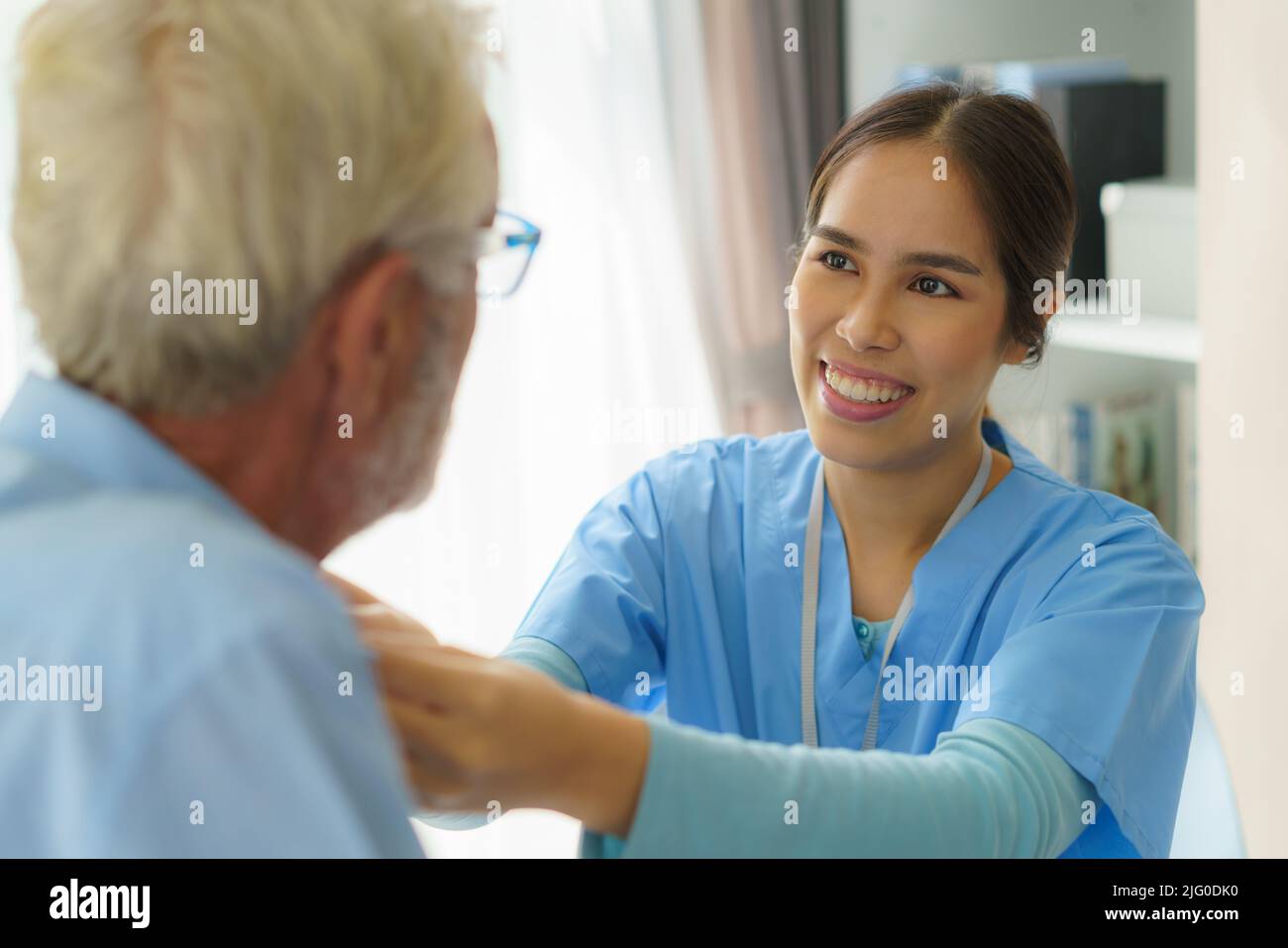 Young Asian woman nurse helping get dress to disabled elderly man in
