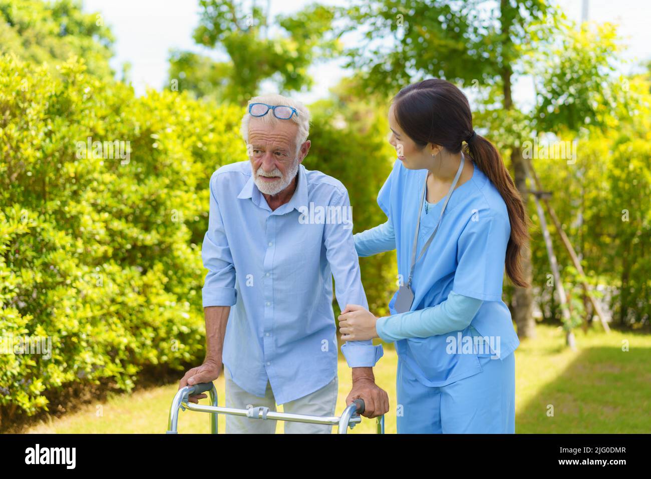 Young Asian woman nurse care giver helping senior old man with mobility walker in garden at home. Senior daycare center, Nurse take care elderly patie Stock Photo