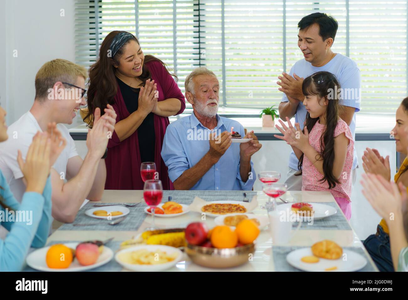 Happy mutiethnicity and multigeneration family celebrating grandfathers birthday in living room at home. Stock Photo