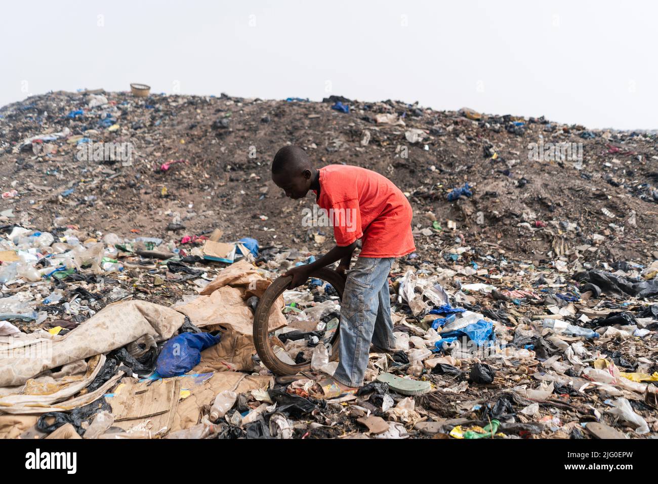 Side view of an African youth standing in a rubbish dump checking if an old bicycle tire he found is still usable to reuse and sell Stock Photo