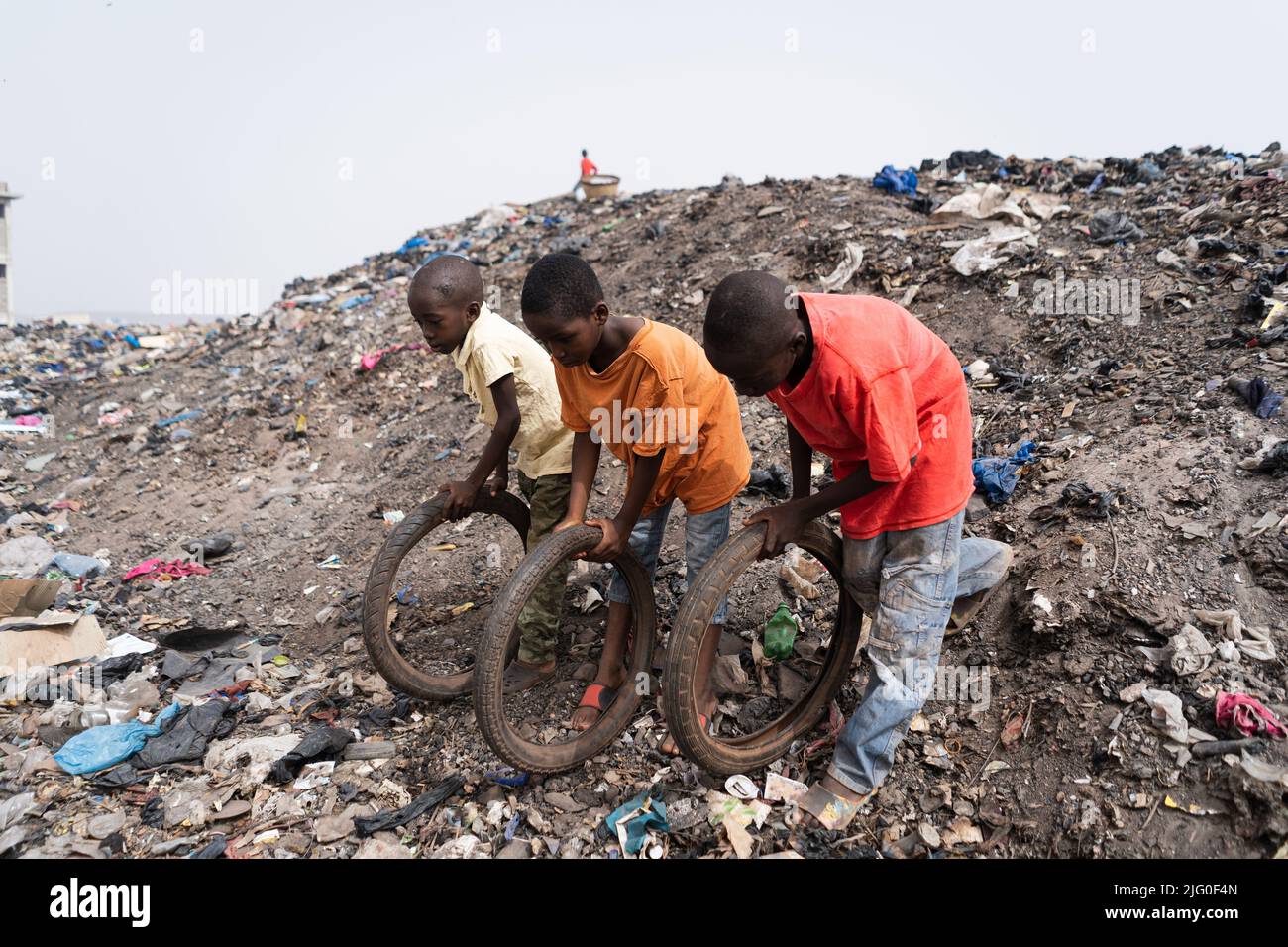 Landfill in West Africa as playground for three little slum boys competing with recycled bicycle tires: poverty concept in developing countries Stock Photo