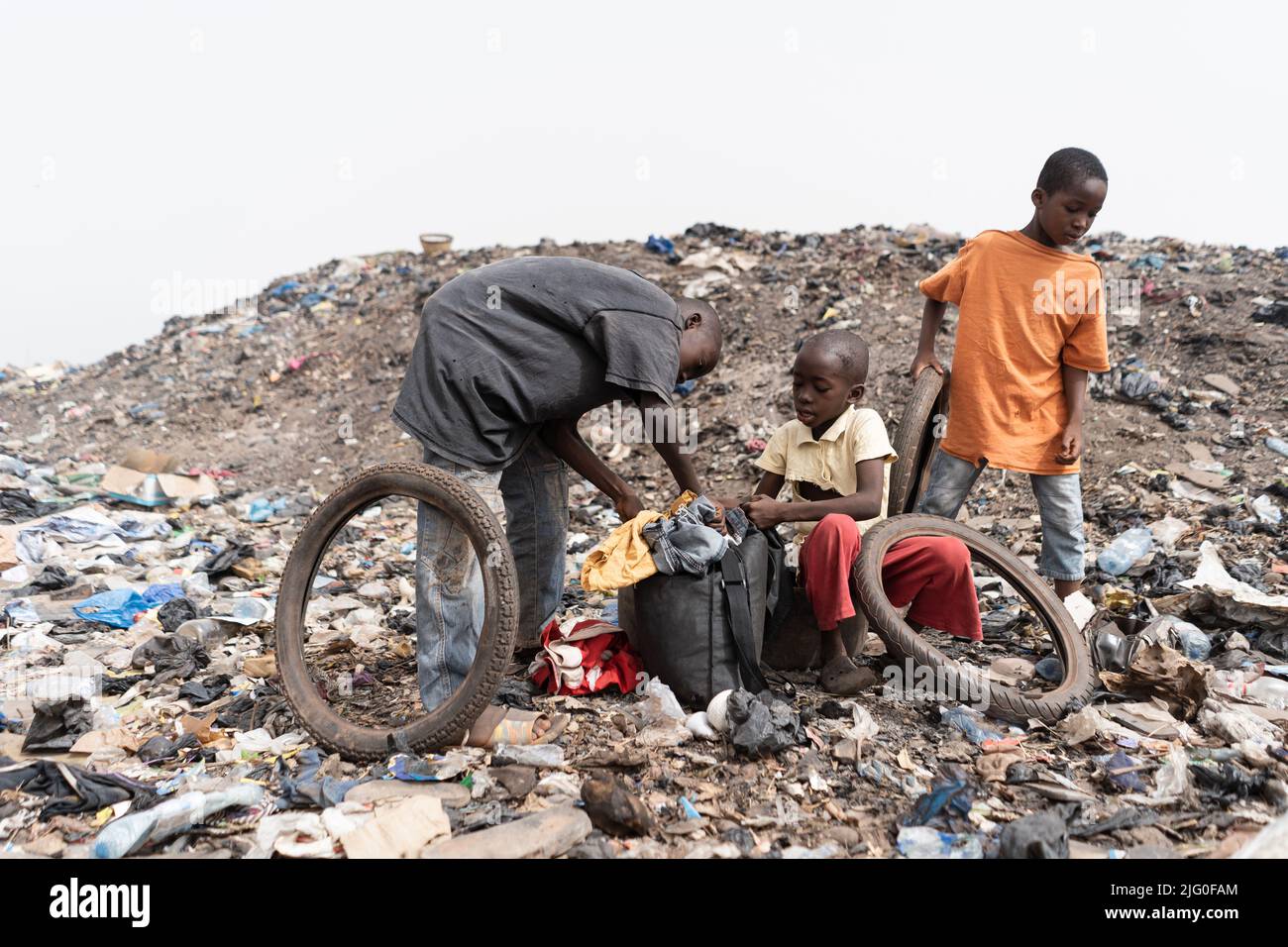 Three homeless street boys in a landfill with their daily loot of garbage to recycle and sell; condition of slum children in Africa Stock Photo
