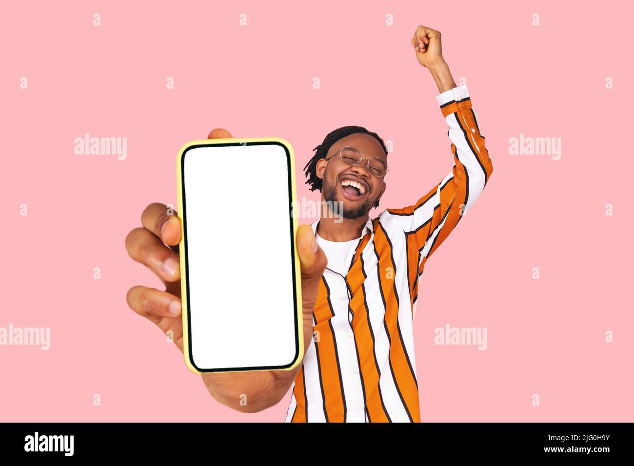 Yes. excited happy celebrating positive bearded a man in striped shirt showing screen on his smartphone mobile cellphone and rejoicing. Indoor studio shot isolated on pink background. Stock Photo