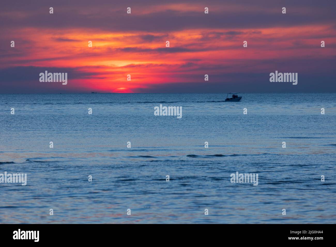 Colorful tropical sunset over the sea with a boat passing Stock Photo