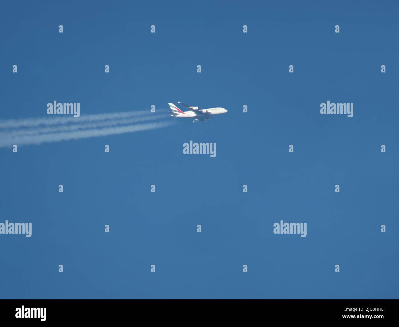 Telephoto view of Emirates Airbus A380 airliner flying at high altitude with contrails Stock Photo
