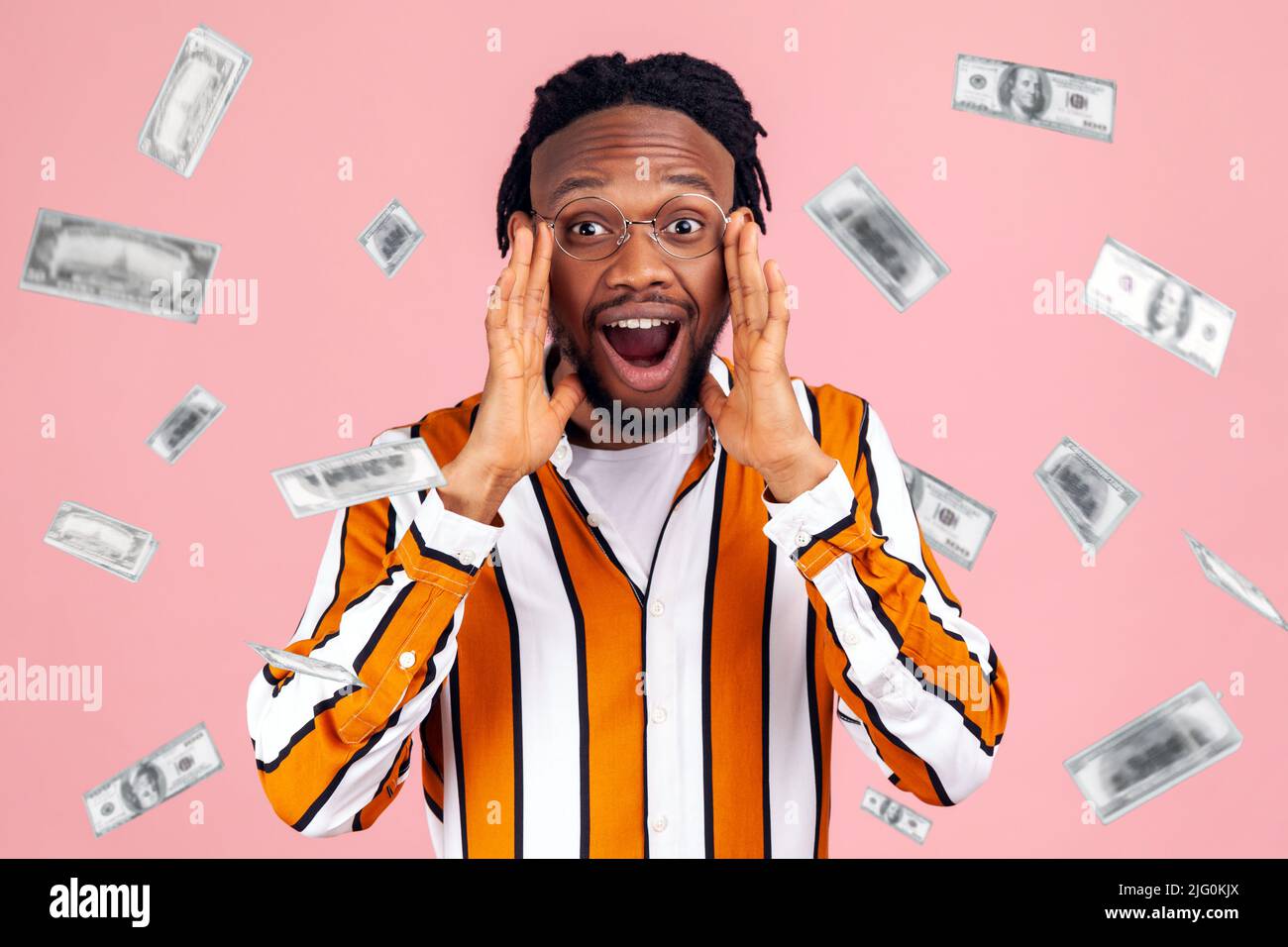 Money rain wow. Bemused surprised rich man looking at camera with overwhelming big eyes, shocked with amazing face. dollars money falling. Indoor studio shot isolated on pink background. Stock Photo