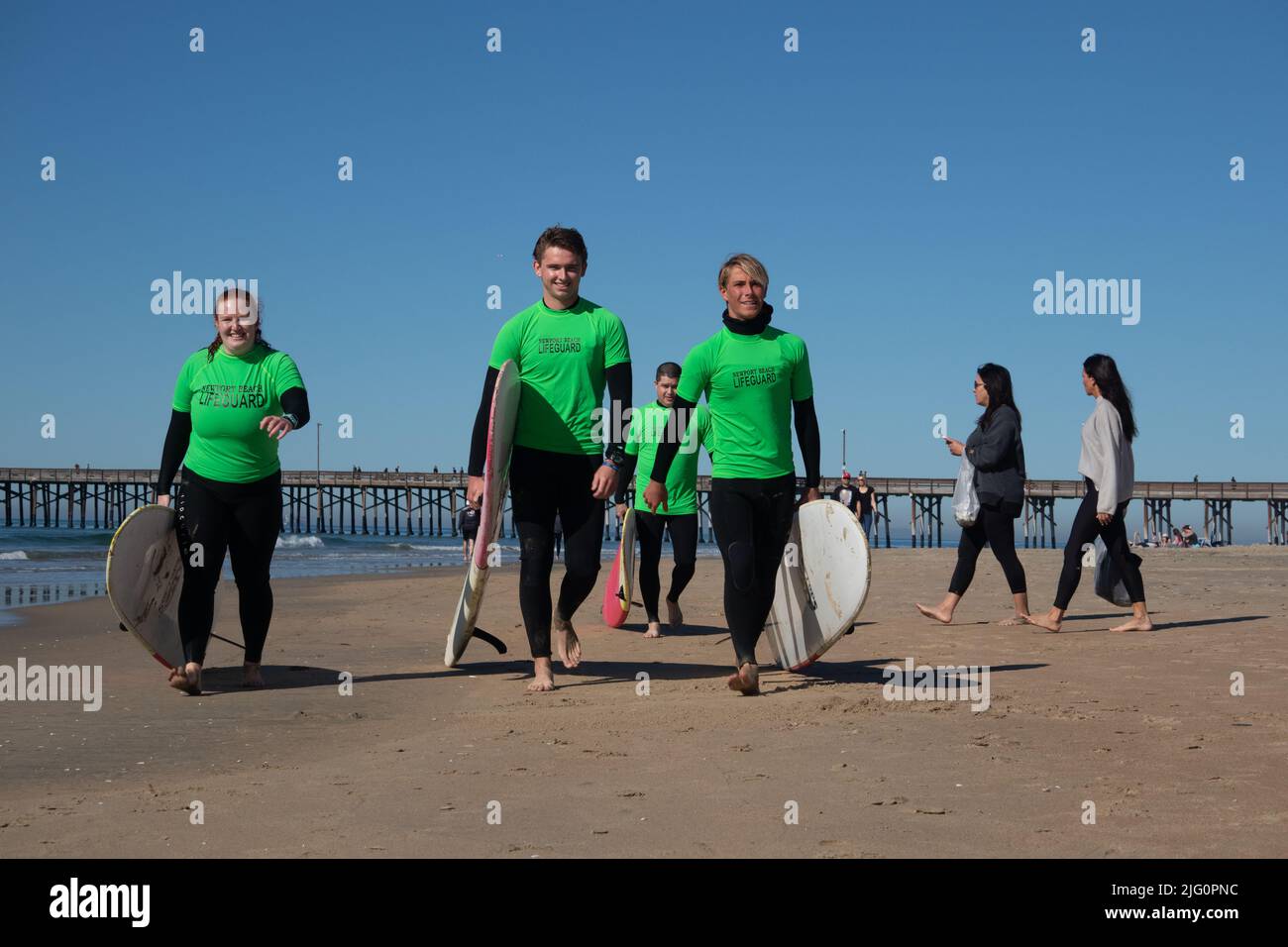 Four young lifeguards wearing green tops carrying surfboards walking proudly along the beach at Newport Beach California USA Stock Photo