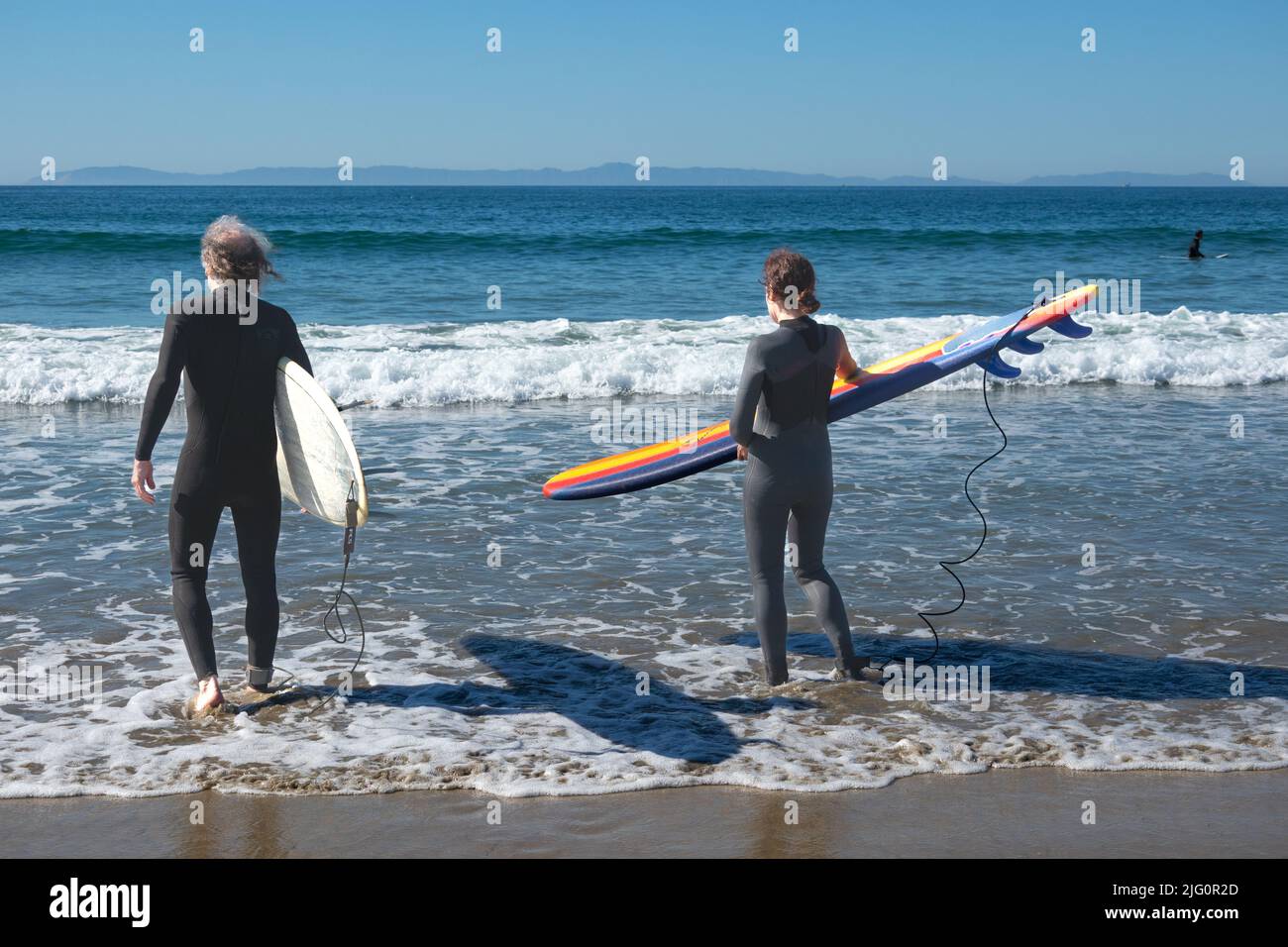 Backs of two older surfers carrying boards into sea Newport Beach Southern Californian USA Stock Photo