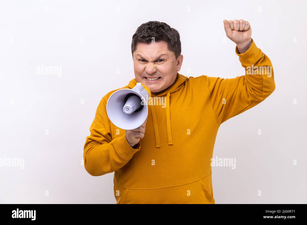 Angry nervous middle aged man loudly screaming at megaphone, making announce, protesting, wants to be heard, wearing urban style hoodie. Indoor studio shot isolated on white background. Stock Photo