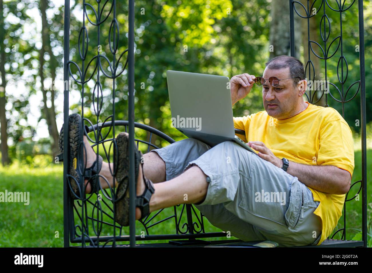 middle aged man with laptop working outside in garden, green home office concept Stock Photo