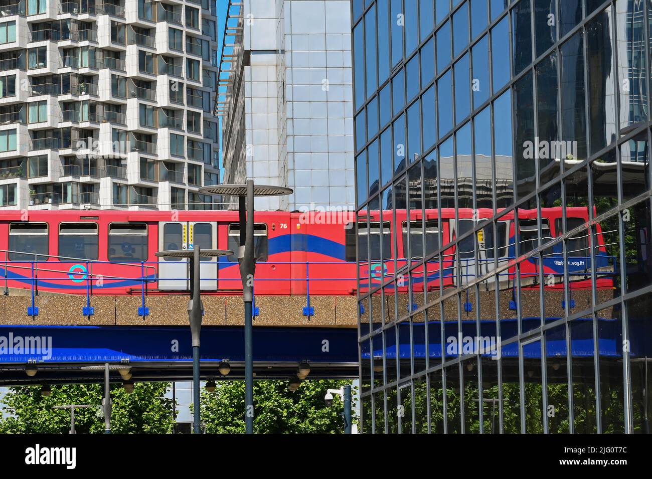 London, England - June 2022: Train on the Docklands Light Railway running on an elevated track with reflection in an office building Stock Photo