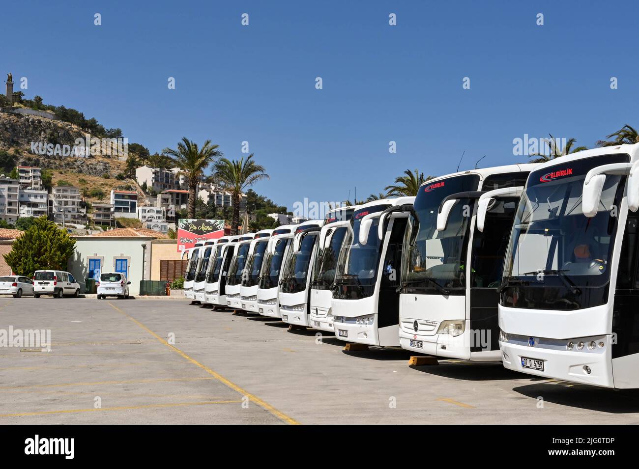 Kusadasi, Turkey - June May 2022: Row of motor coaches waiting for passengers from a cruise ship. In the background is a sign on the hill Stock Photo