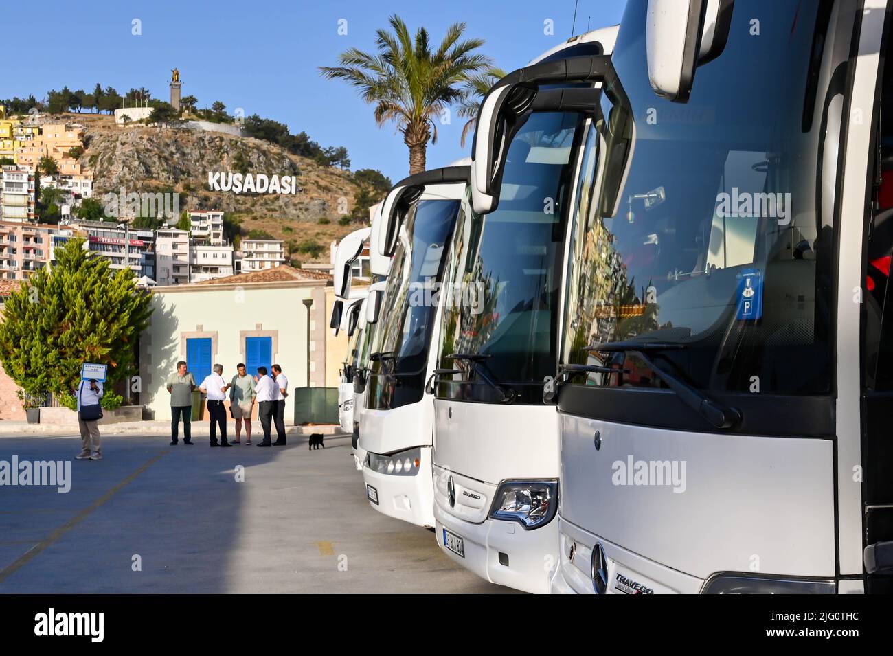 Kusadasi, Turkey - June May 2022: Row of motor coaches waiting for passengers from a cruise ship. In the background is a sign on the hill Stock Photo