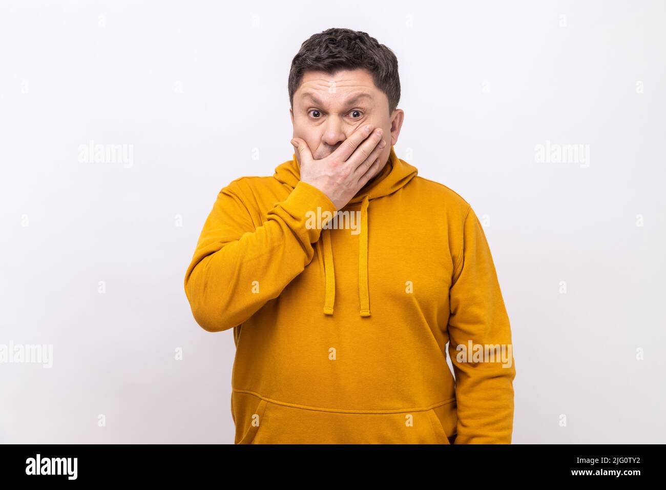 I won't say anyone. Portrait of confused man covering mouth with hand, keeping terrible secret truth, don't want to talk, wearing urban style hoodie. Indoor studio shot isolated on white background. Stock Photo