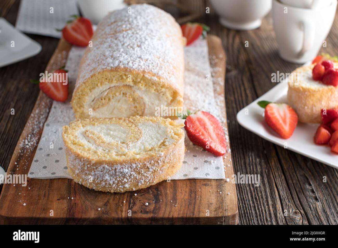 Biscuit roll or swiss roll with whipped cream filling and strawberries Stock Photo