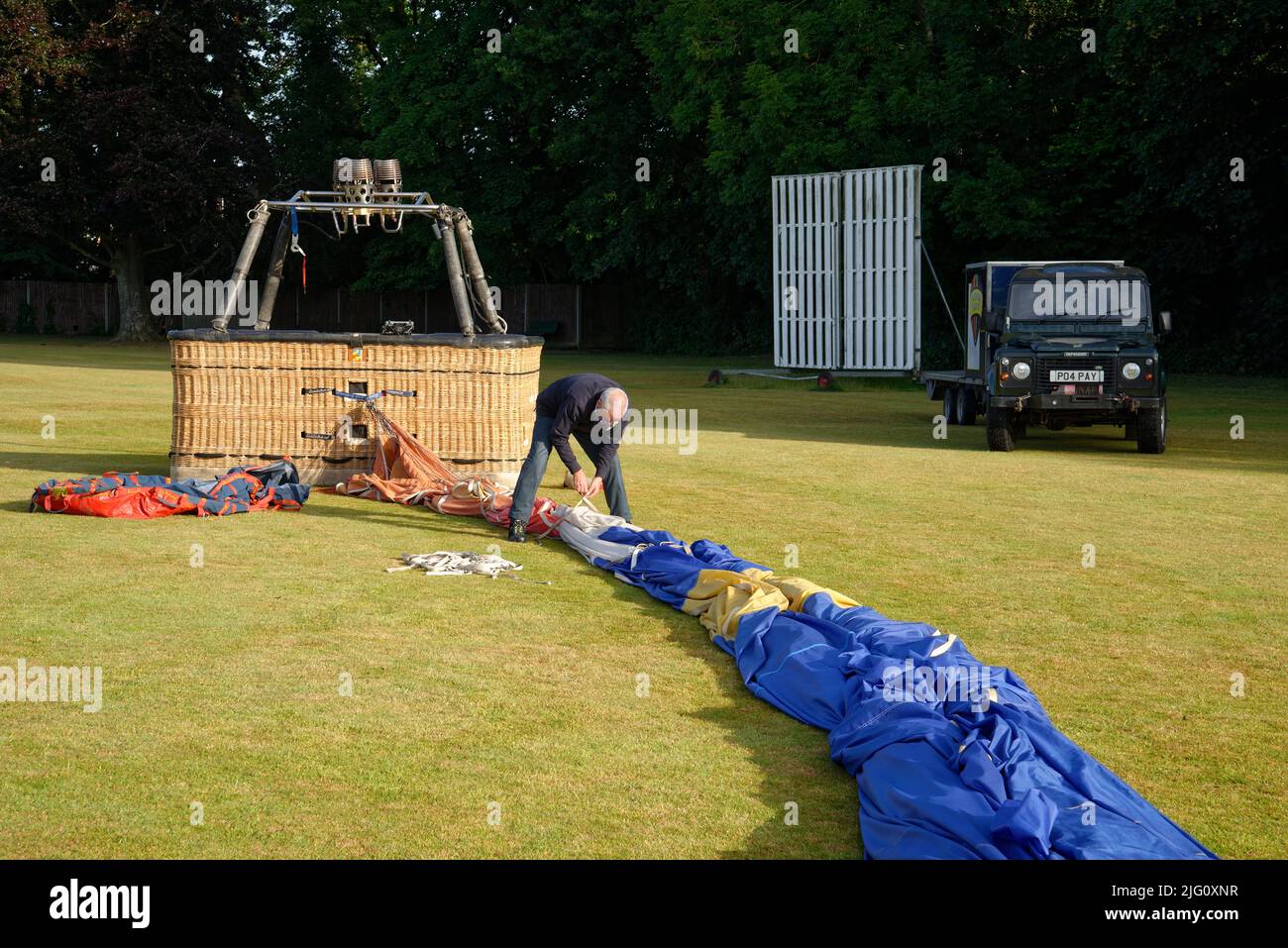 A hot air balloon. Putting the balloon away after landing near a cricket pitch. The gondola (basket) and the folded envelope (balloon fabric). Stock Photo