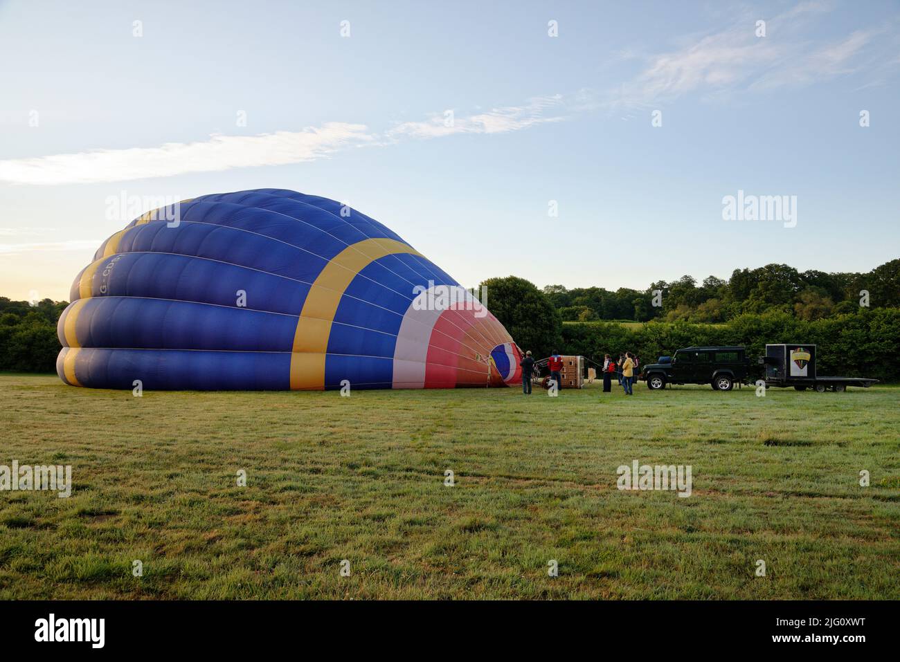 A hot air balloon. Getting the balloon (or envelope) filled with air prior to take off. Morning sunrise in a field. Stock Photo