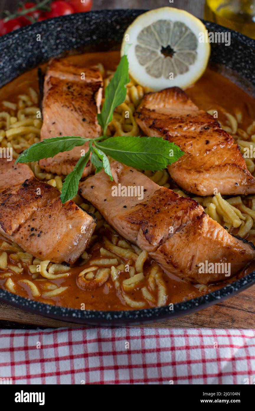 Pan fried salmon fillet with tomato cream sauce and spaetzle noodle. Savory fish dish Stock Photo