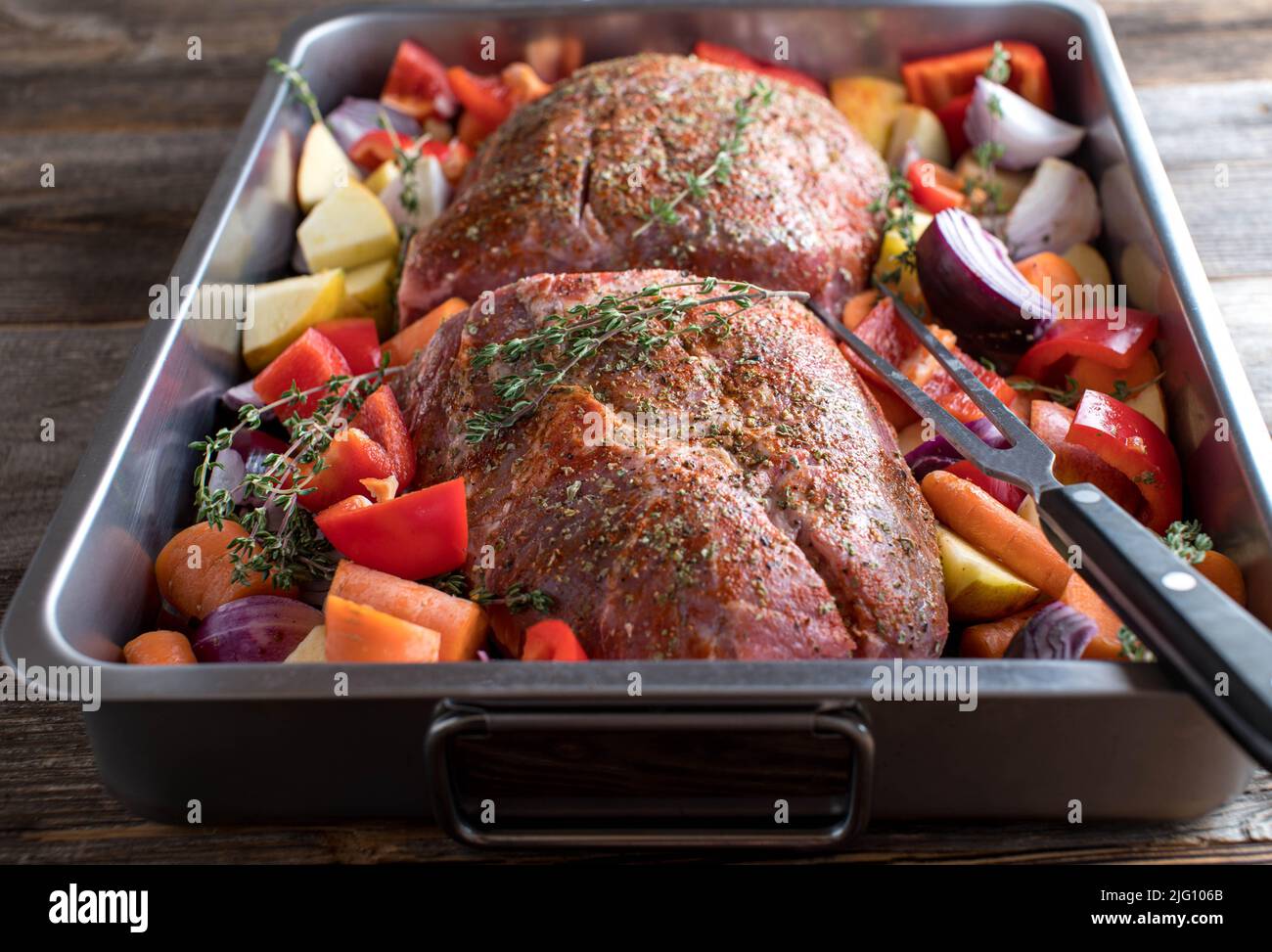 Roast pork raw and uncooked with vegetables in a roasting pan