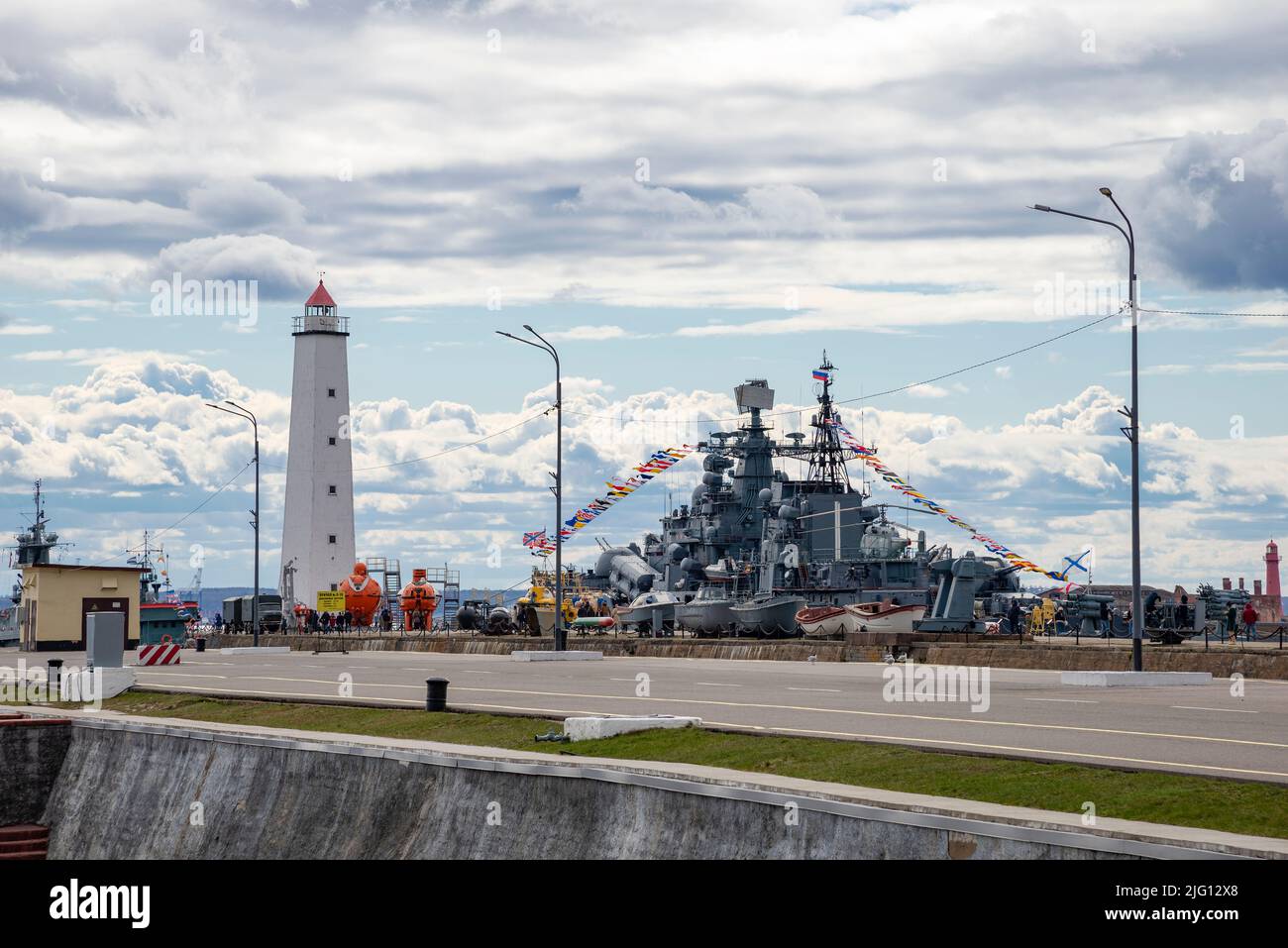 KRONSTADT, RUSSIA - MAY 01, 2022: View of an ancient lighthouse and a moored warship in the Petrovsky Canal. Kronstadt Stock Photo