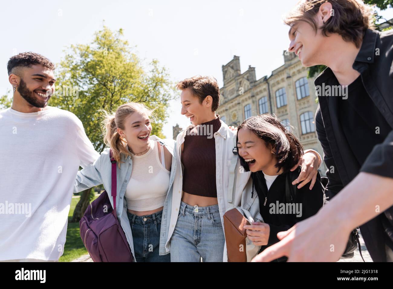 Smiling student hugging interracial friends with backpacks outdoors Stock Photo