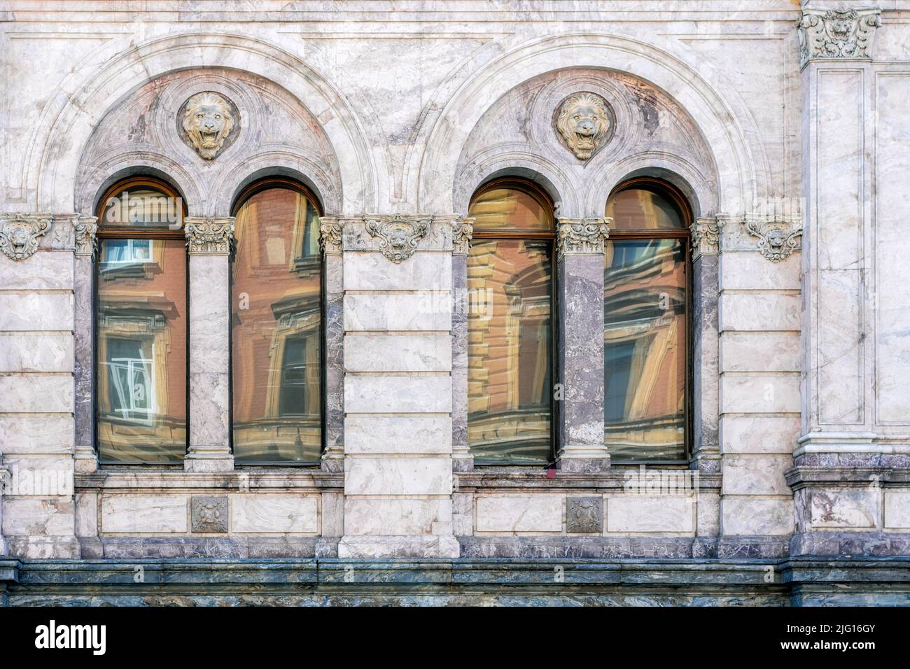 Four arched windows with a bas-relief of a lion's head against a marble stone wall. From the Windows of the world series. Stock Photo