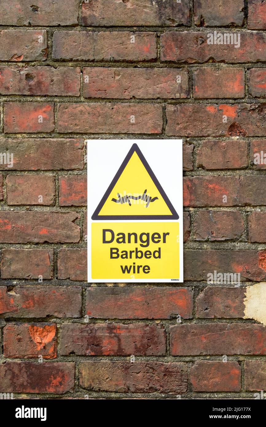 Warning barbed wire sign on red brick wall Stock Photo