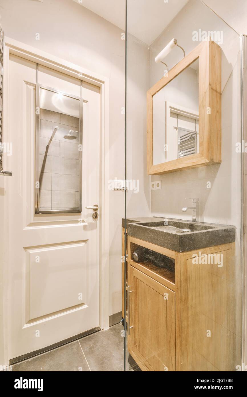 Cupboard with sink and mirror attached to tiled wall near door and