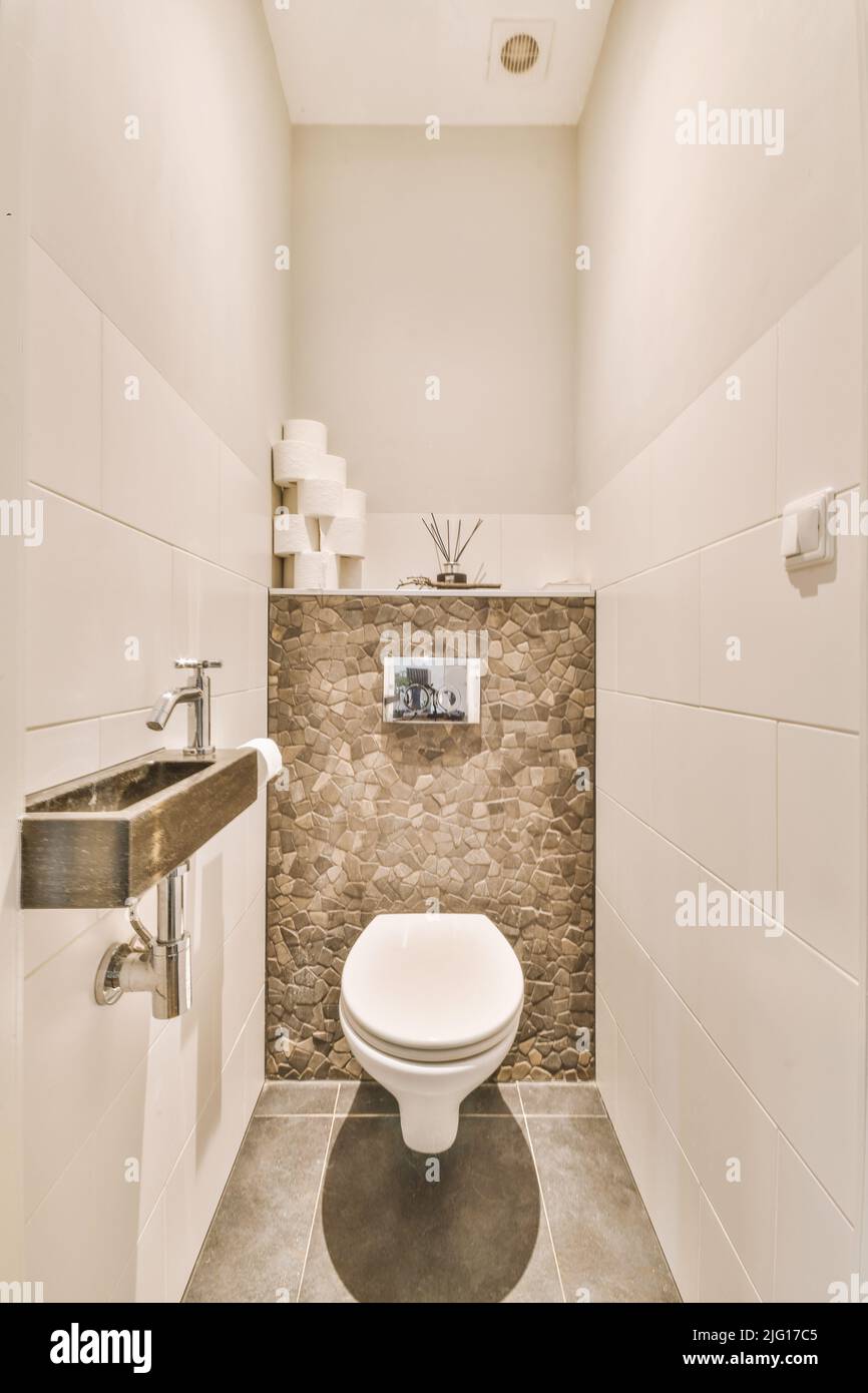 Wall hung toilet and small sink in corner in lavatory room with beige