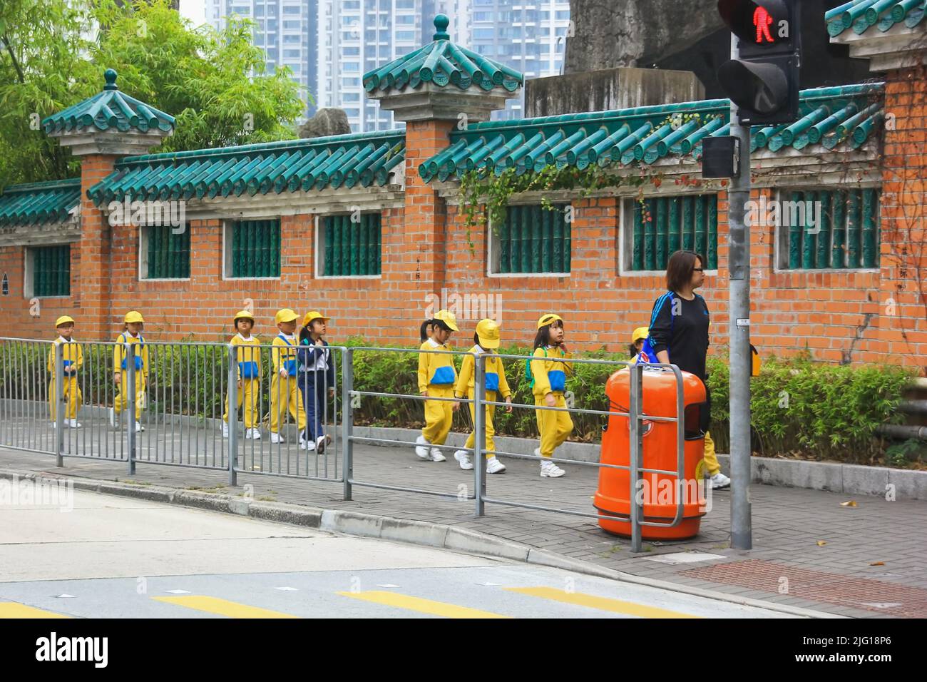 Group of elementary school students are walking to excursion with teachers along ancient Buddhist temple wall. Hong Kong Stock Photo