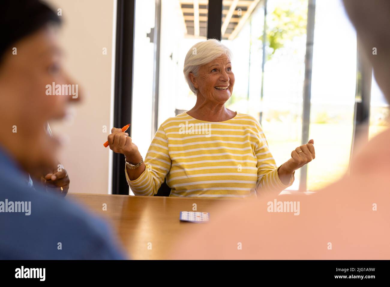 Cheerful biracial senior woman gesturing while playing bingo at dining table in nursing home Stock Photo