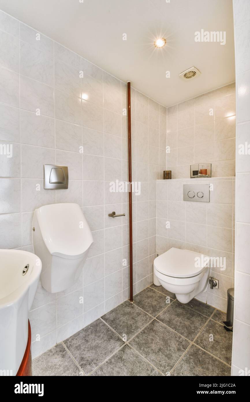 Interior of narrow restroom with sink and wall hung toilet with white