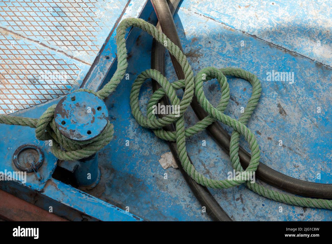 A short length of pale green mooring rope tied to a small single bollard on the deck of a ship painted pale blue Stock Photo
