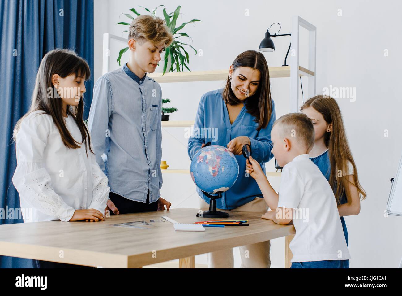 Teacher and children in class are looking at globe, teacher helps explain the lesson to the children in the class at a desk. Educational school proces Stock Photo