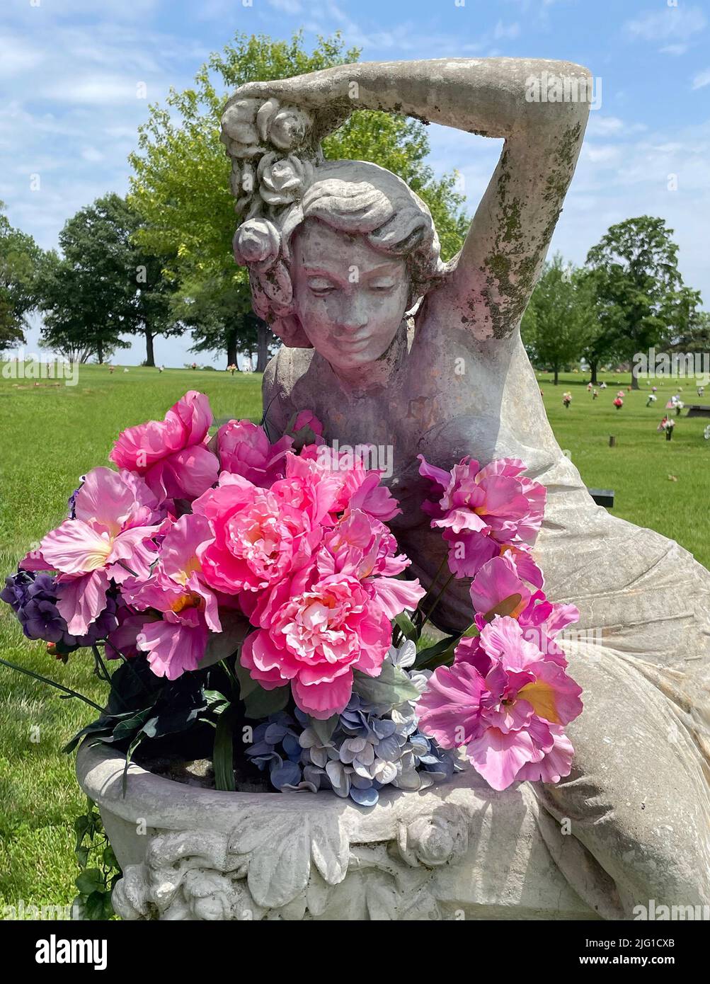 Statue of maiden holding flowers in cemetery. Stock Photo