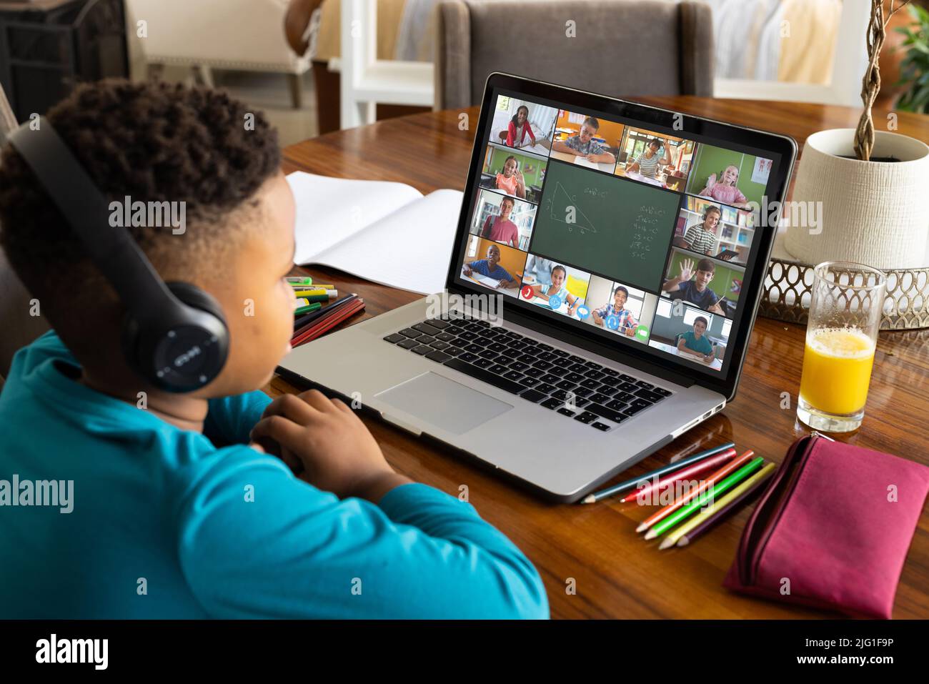 Biracial boy wearing headphones and looking at laptop screen while attending online class at home Stock Photo