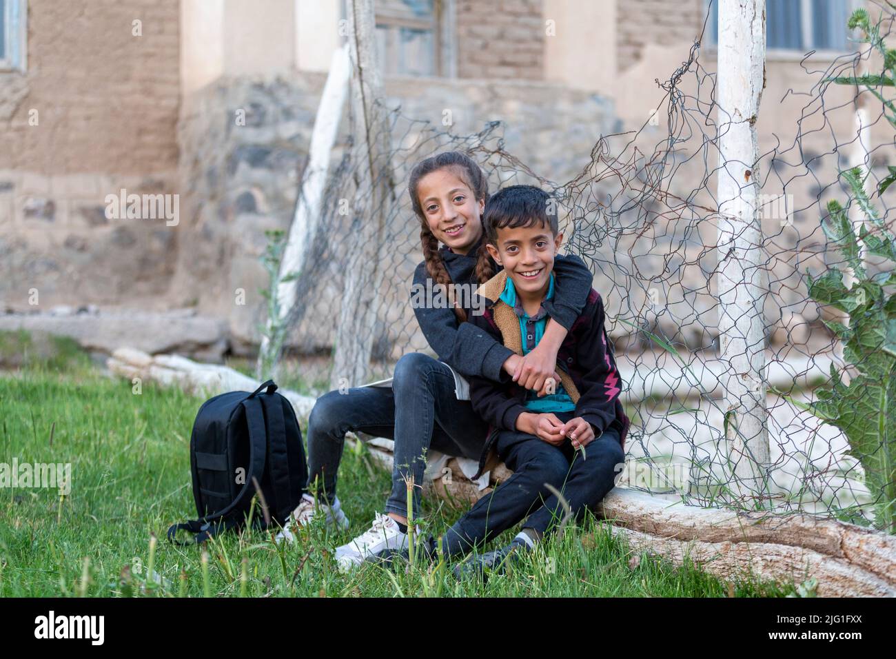 Two refugee brothers and sisters are sitting next to a child-braided fence. Stock Photo