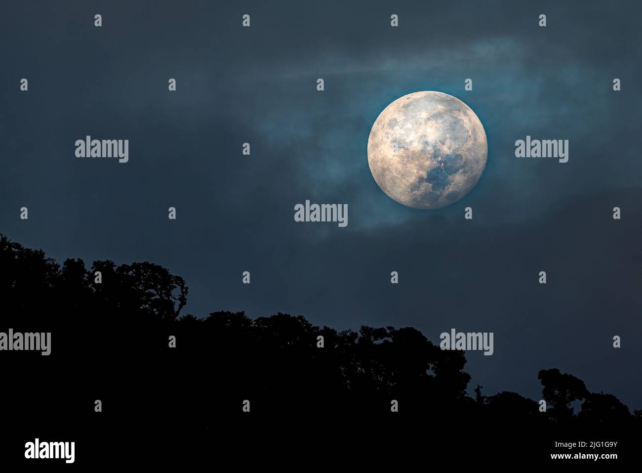 Full moon setting big in the sky shining trough some dark clouds over cloud forest Stock Photo