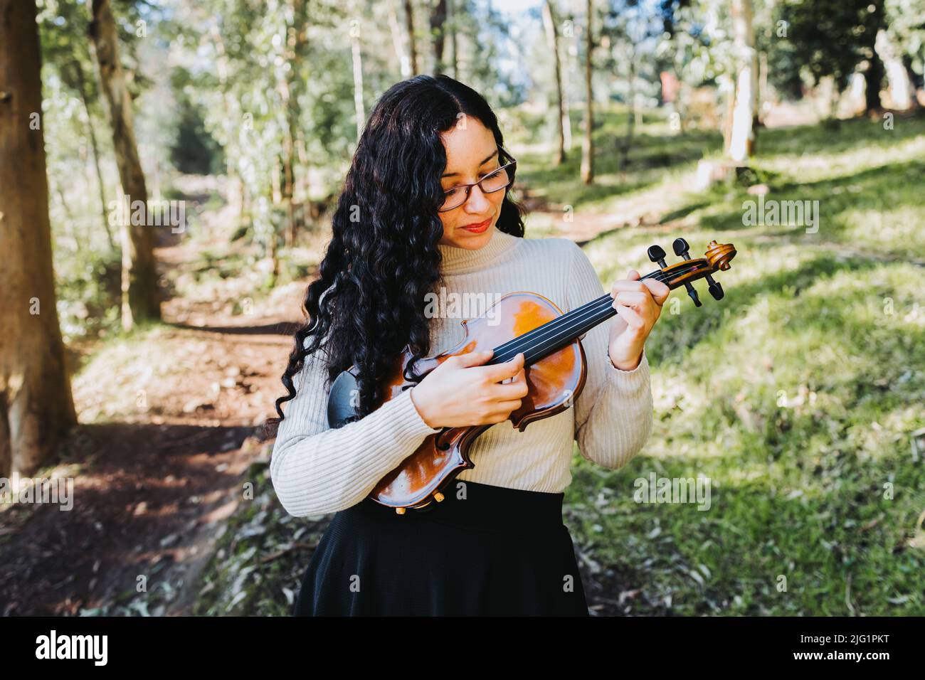 curly brunette woman using glasses and doing pizzicato technique in violin. Selective focus. Stock Photo