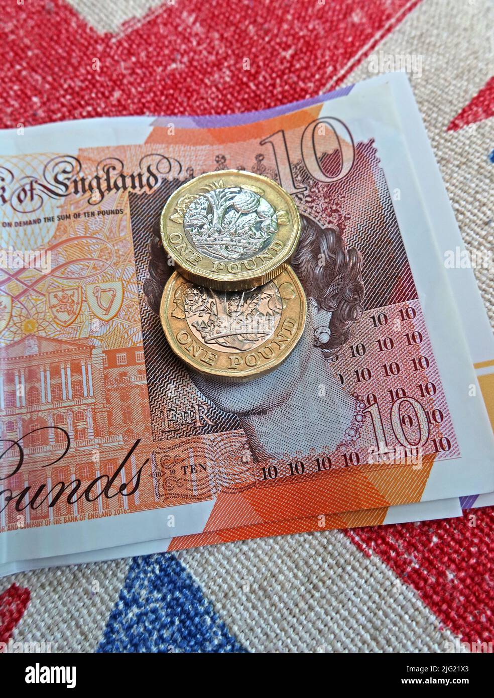 Sterling pound notes, bank of England and pound coins on a union jack flag - cost of living crisis, in UK / GB Stock Photo