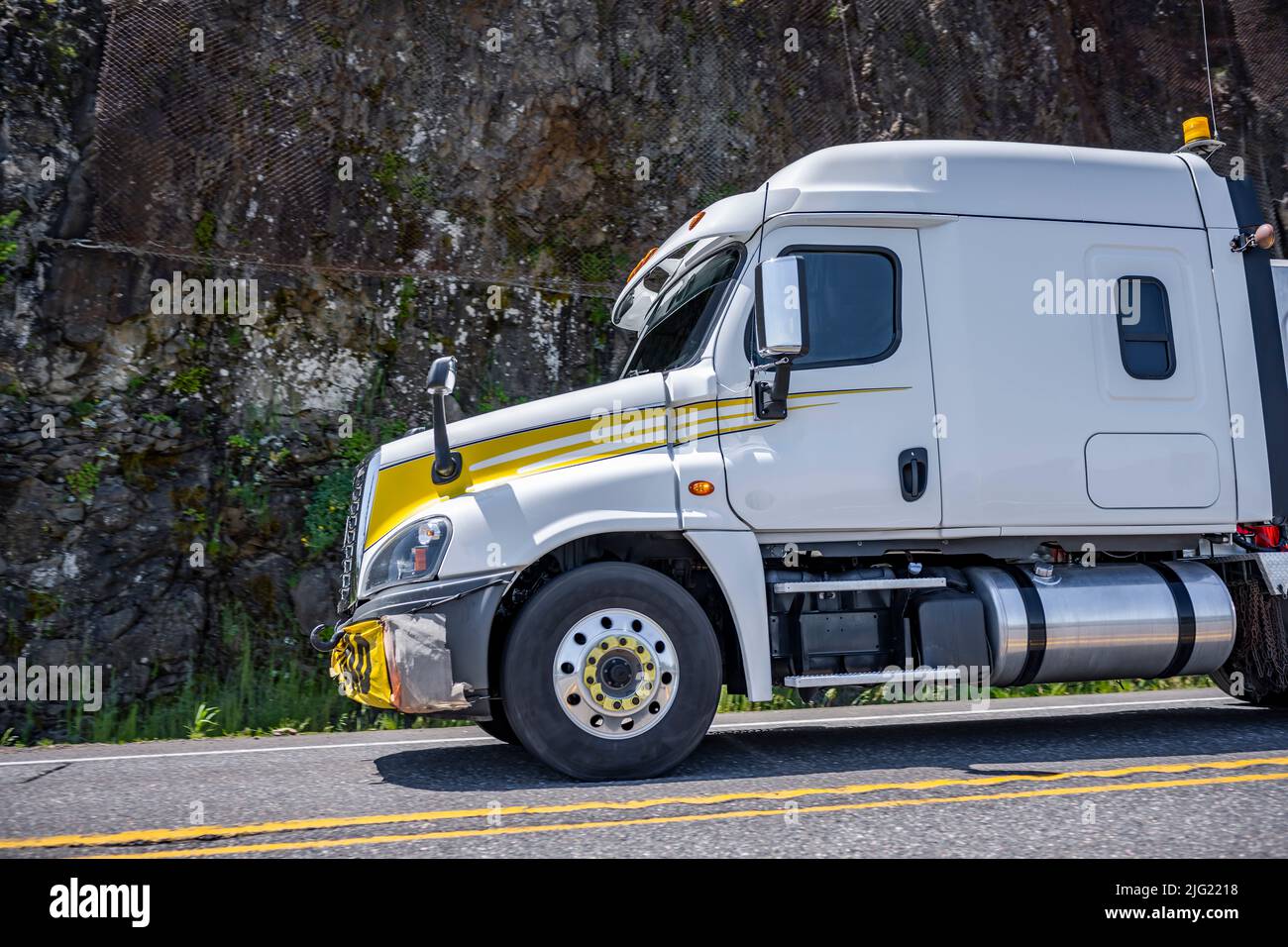 Low cab profile to improve aerodynamics big rig white semi truck tractor with oversize load sign on the bumper and flashing lights on the roof running Stock Photo