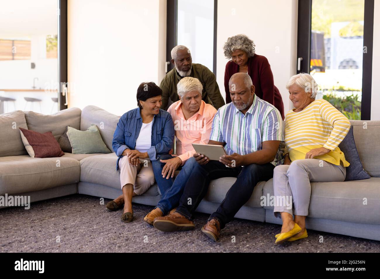 Multiracial seniors looking at digital tablet using by male friend while sitting on sofa Stock Photo