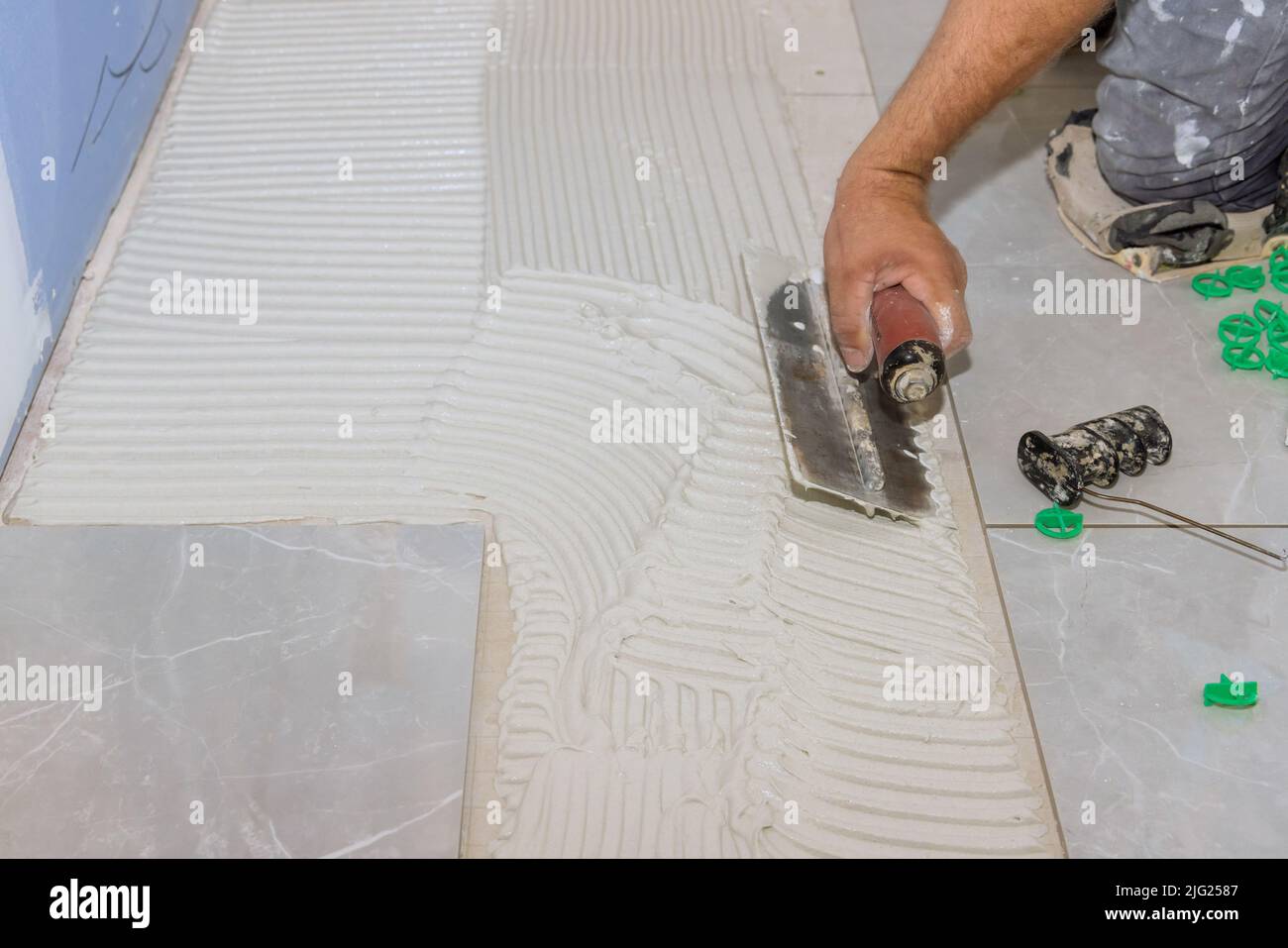 Using trowels to apply adhesive to concrete floors before tilelaying