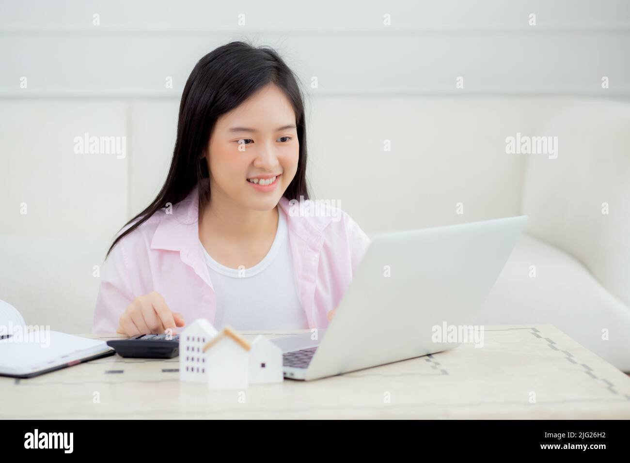 Young asian woman sitting and planning and calculate expense and mortgage with calculator and home on desk, insurance and budget of residential, loan Stock Photo