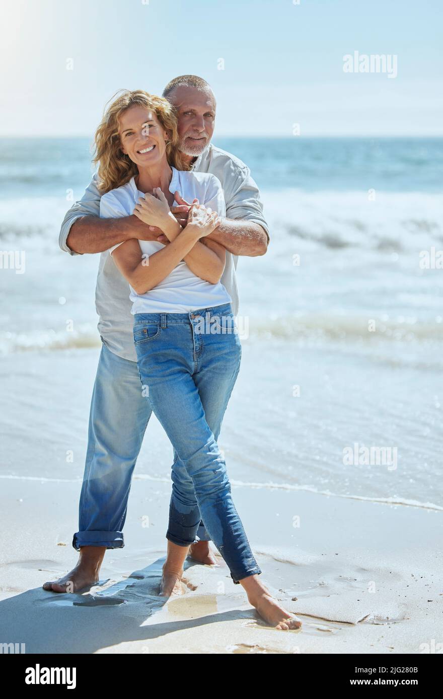 Portrait of a happy and loving mature couple enjoying a day at the beach in summer. Cheerful affectionate senior husband hugging his joyful wife while Stock Photo
